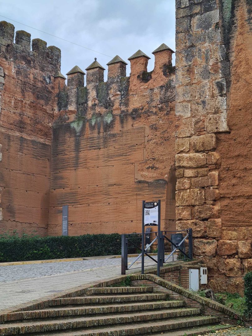 Einblick durch die Stadtmauer von Niebla, begleitet von einer Infotafel mit Erklärungen – Wohnmobil-Rundreise Spanien