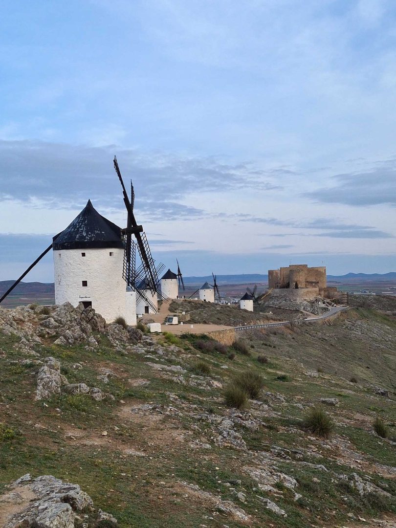 Fünf Windmühlen stehen auf einem Hügel, im Hintergrund ragt das Kastell von Consuegra empor – Wohnmobil-Rundreise Spanien